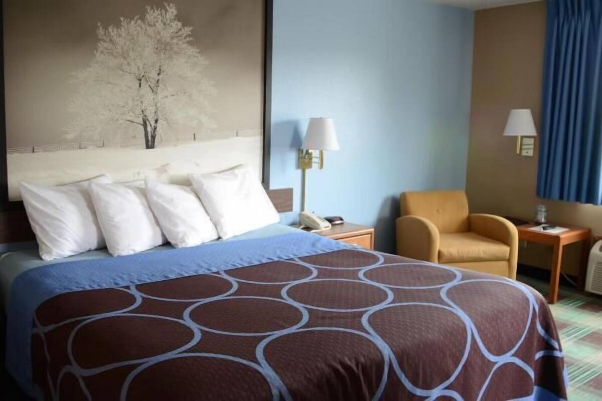 A hotel room with a large bed, two bedside tables, a chair, and a painting on the wall.