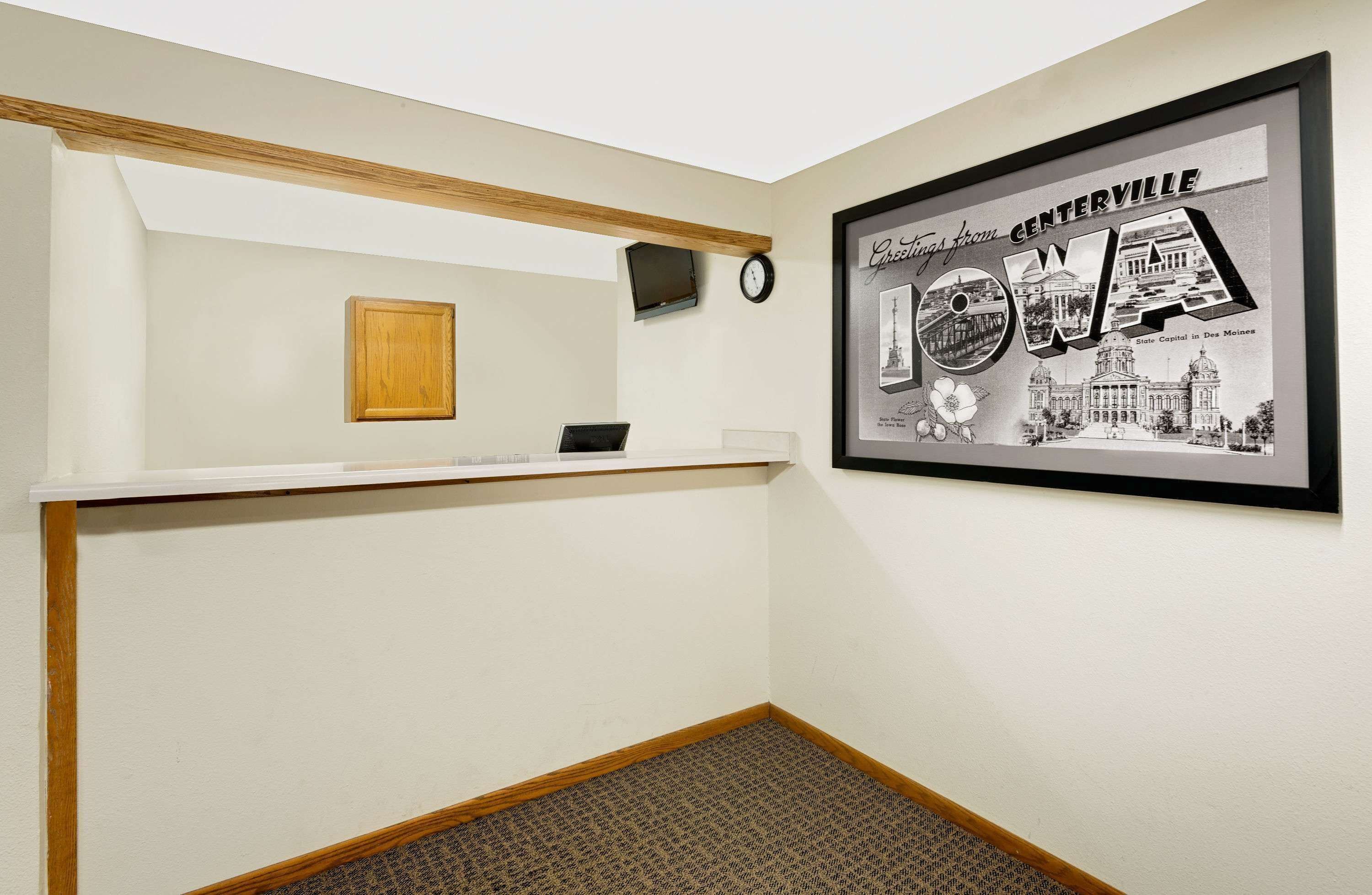 Un hall d’hôtel avec un comptoir d’accueil, une horloge et un tableau représentant un paysage de l’Iowa.