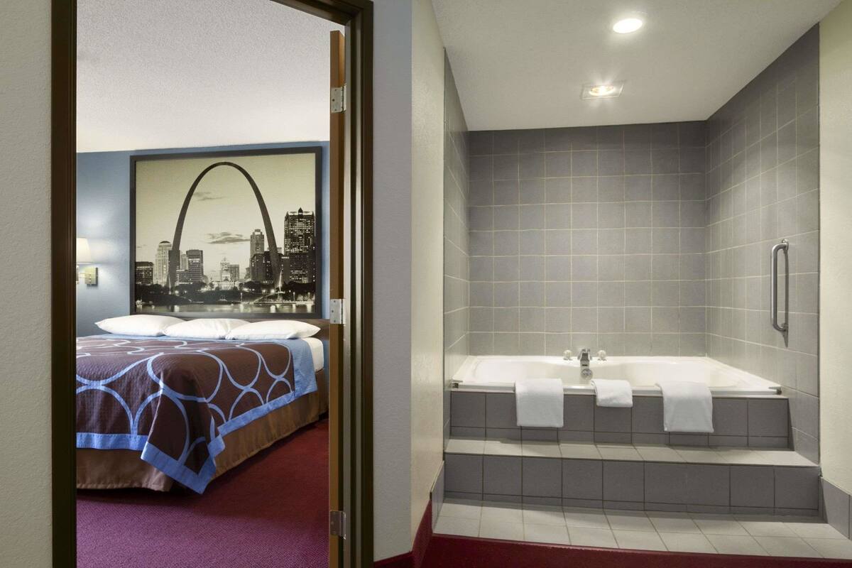 A hotel room with a bed, a cityscape mural, and a bathroom with a bathtub and tiled walls.