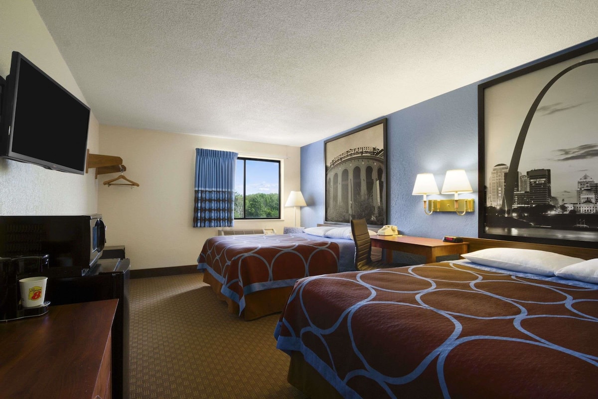 A hotel room with two beds, a TV, a desk with a lamp, and a window with curtains.
