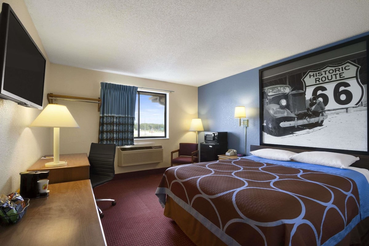 A hotel room with a bed, desk, chair, television, and a wall mural of Historic Route 66.