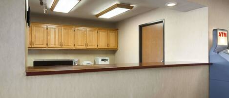 A hotel reception area with wooden cabinets, a microwave, a cash register, and an ATM.