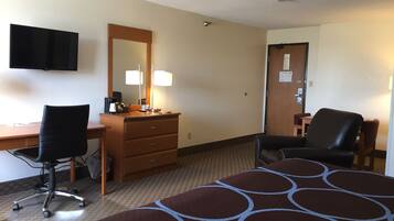 A hotel room with a bed, a desk with a chair, a dresser, a mirror, and a television.