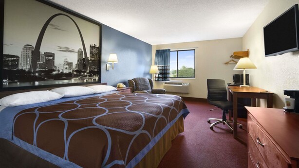 A hotel room with a large bed, a desk with a computer, a chair, a TV, and a window with a view of buildings.