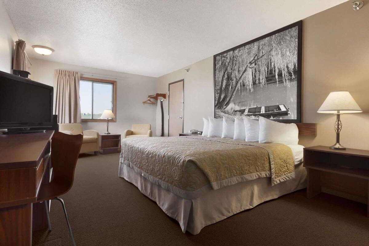 A hotel room with a bed, a desk, a chair, a television, a lamp, and a large painting on the wall.
