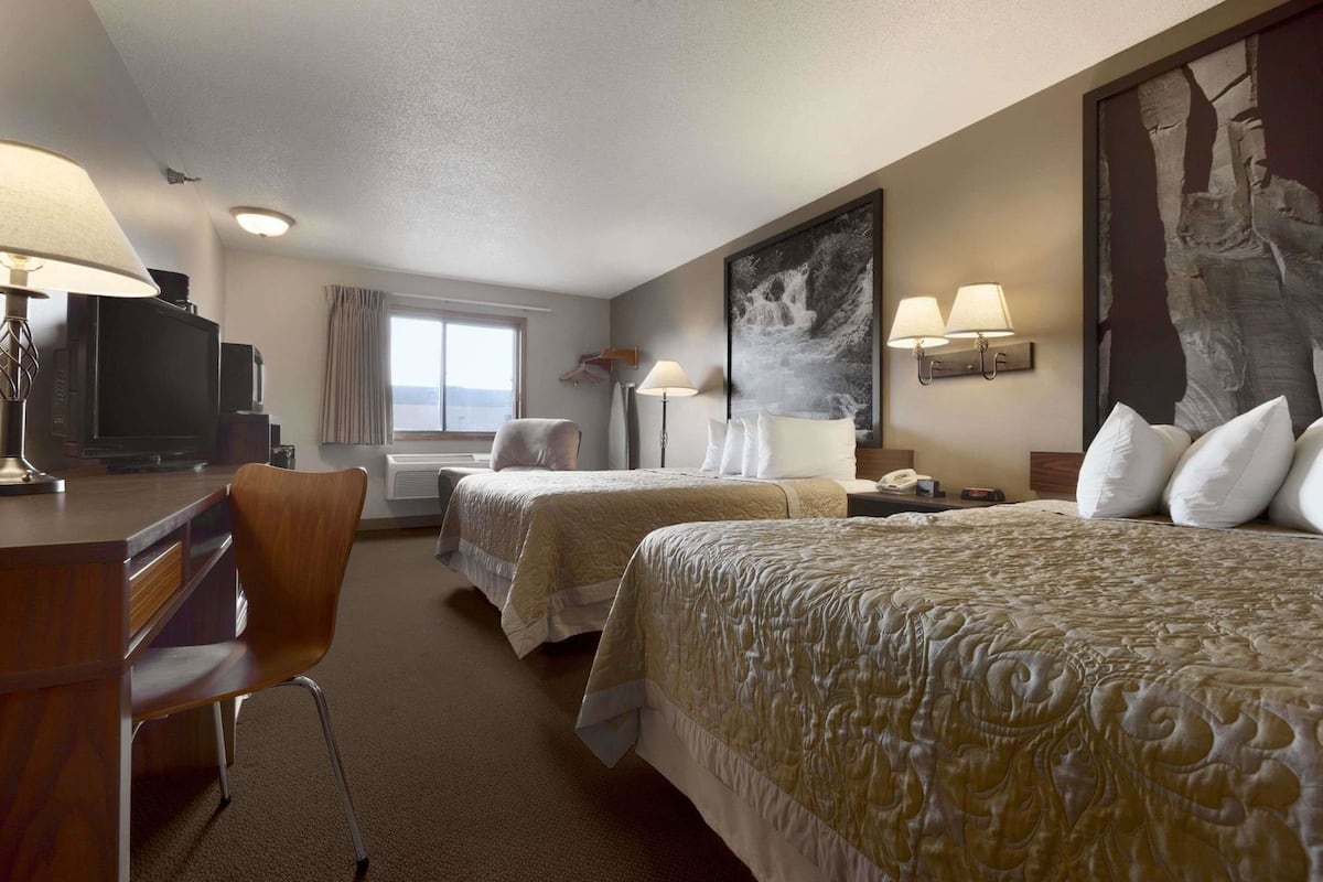A hotel room with two beds, a desk, a chair, a TV, and a large painting on the wall.