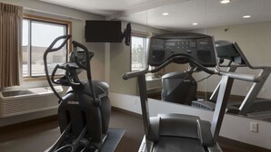 Un gimnasio con una máquina elíptica, una cinta de correr y un espejo grande.