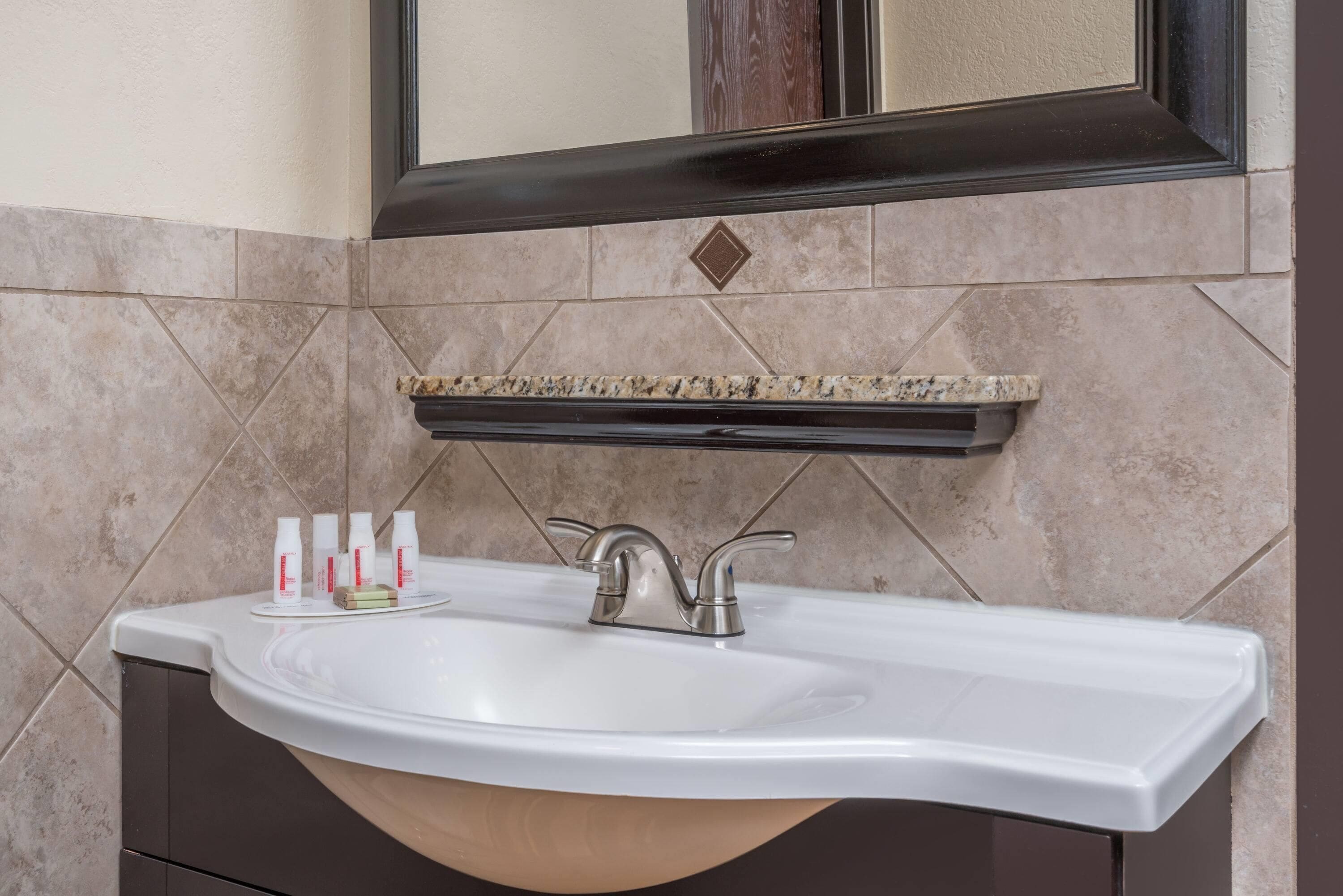 A bathroom with a white sink, a mirror above it, and a shelf with toiletries.