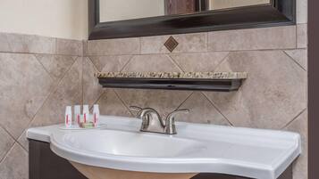 A bathroom with a white sink, a mirror above it, and a shelf with toiletries.