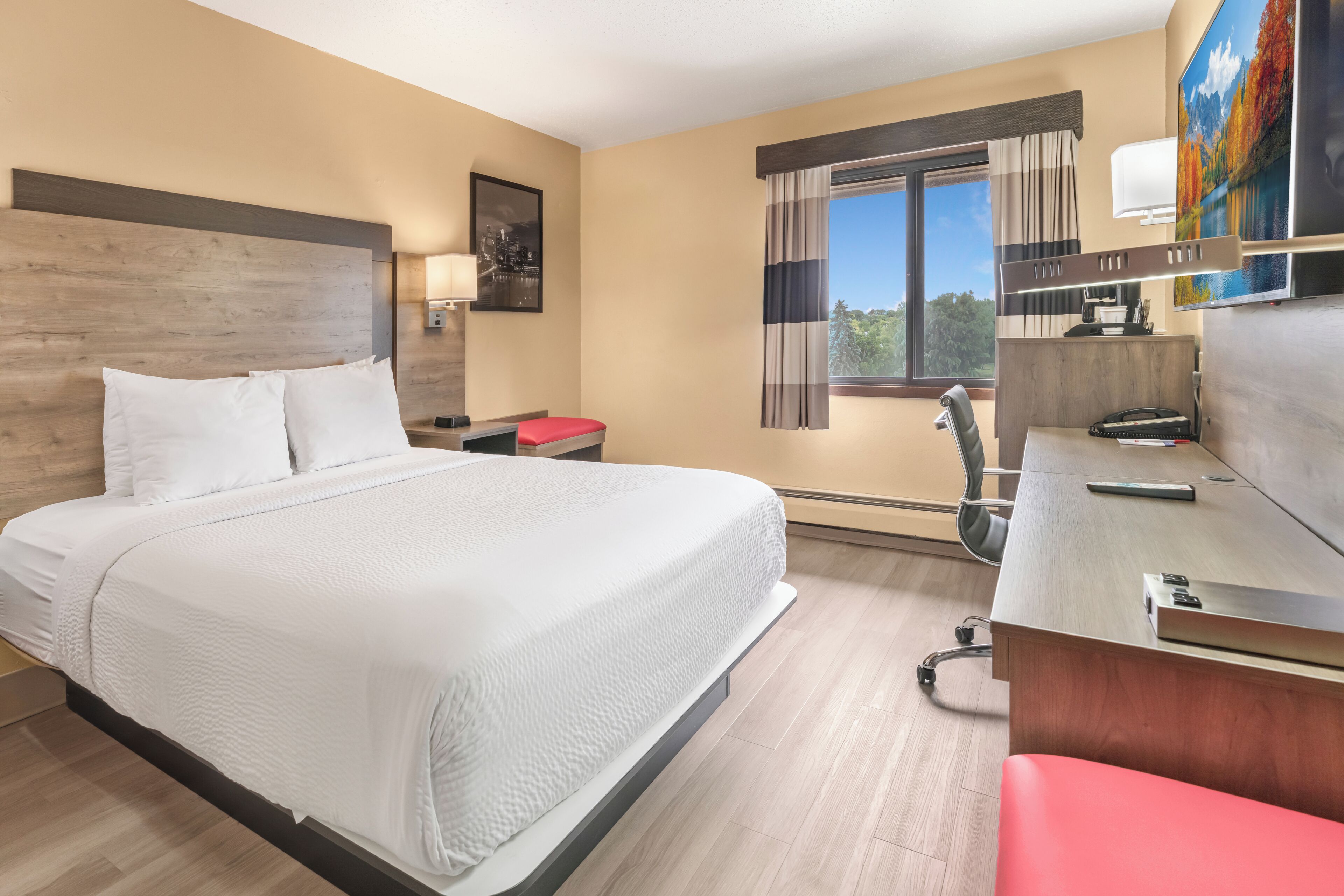 Une chambre d’hôtel avec un grand lit, un bureau avec un ordinateur, une chaise et une fenêtre avec des rideaux.