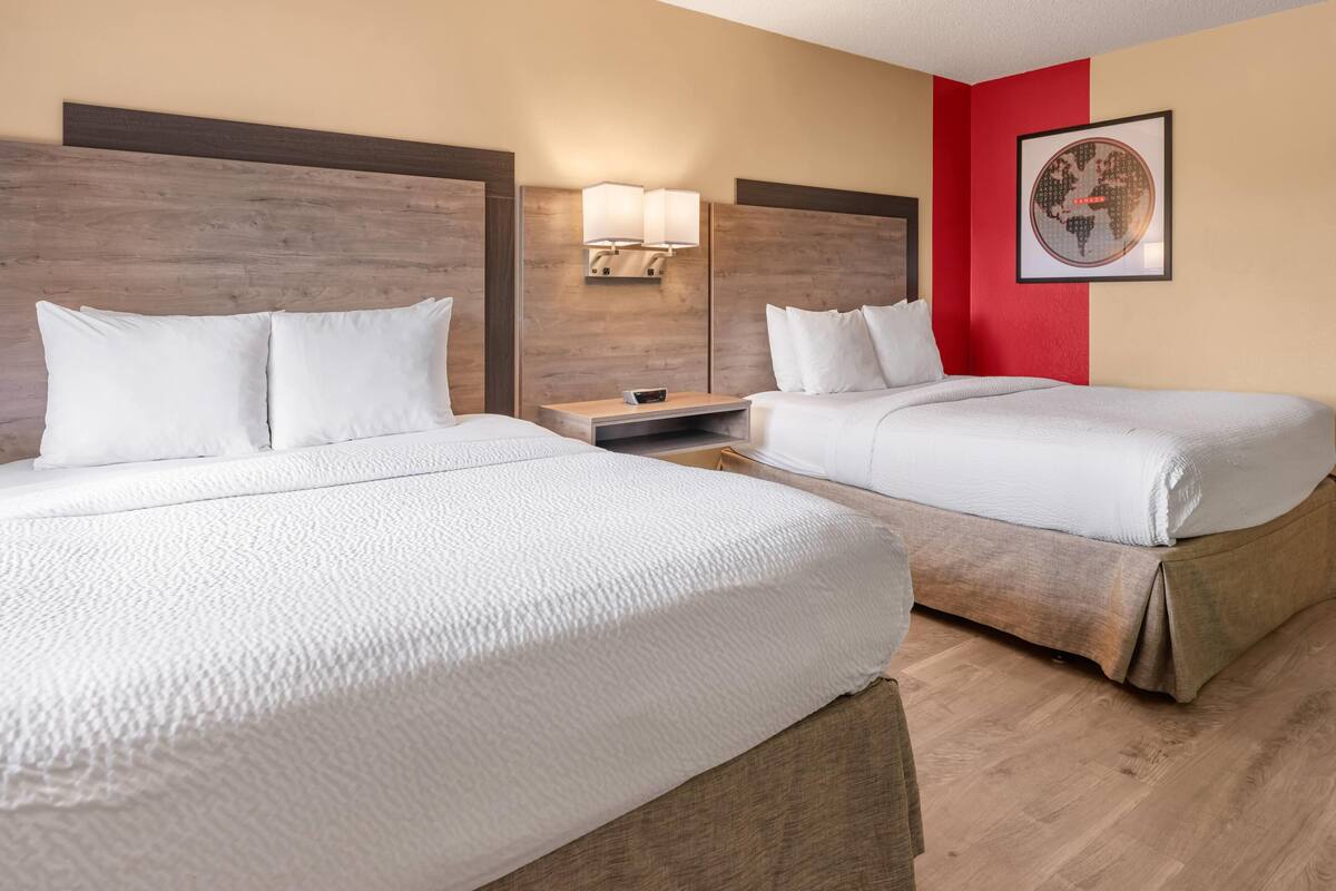 A hotel room with two beds, a nightstand, a lamp, and a framed picture on the wall.