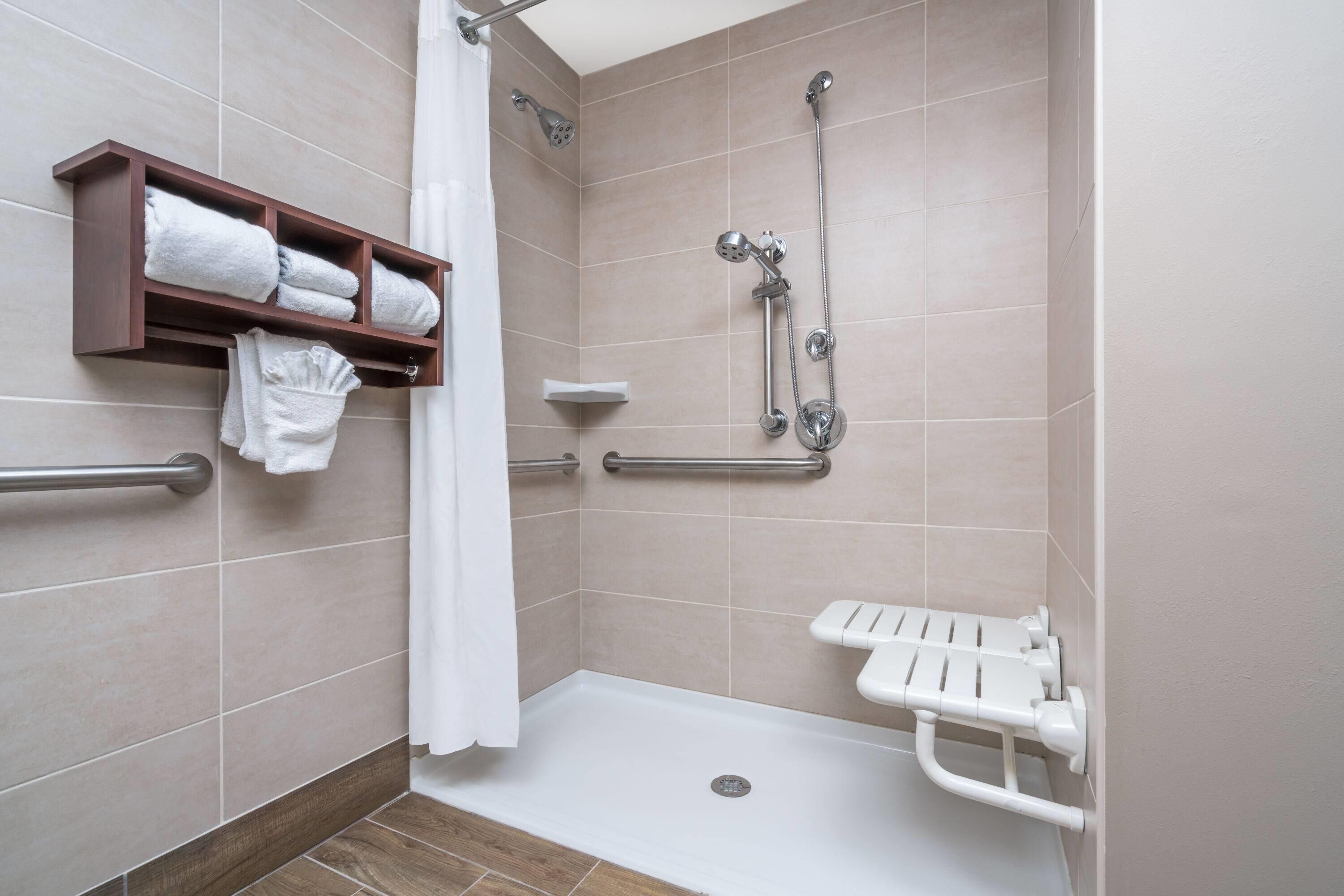 A shower area with a grab bar, a shelf with towels, and a white shower seat.