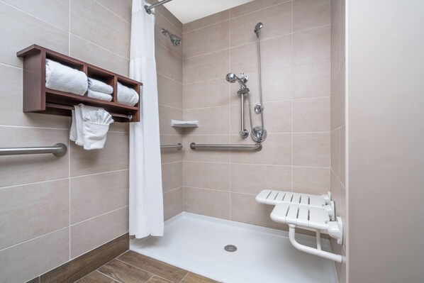 A shower area with a grab bar, a shelf with towels, and a white shower seat.