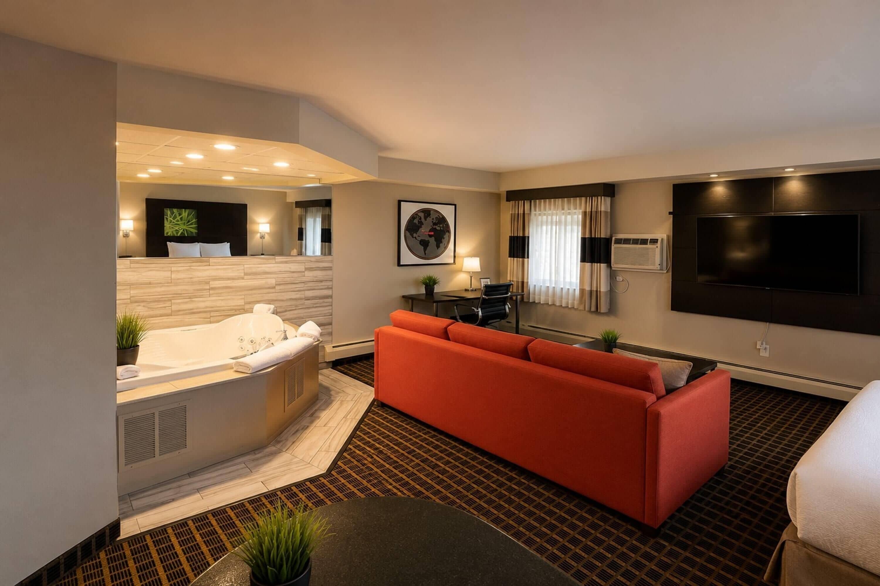 A modern hotel room with a large bed, a red sofa, a flat-screen TV, and a small table.