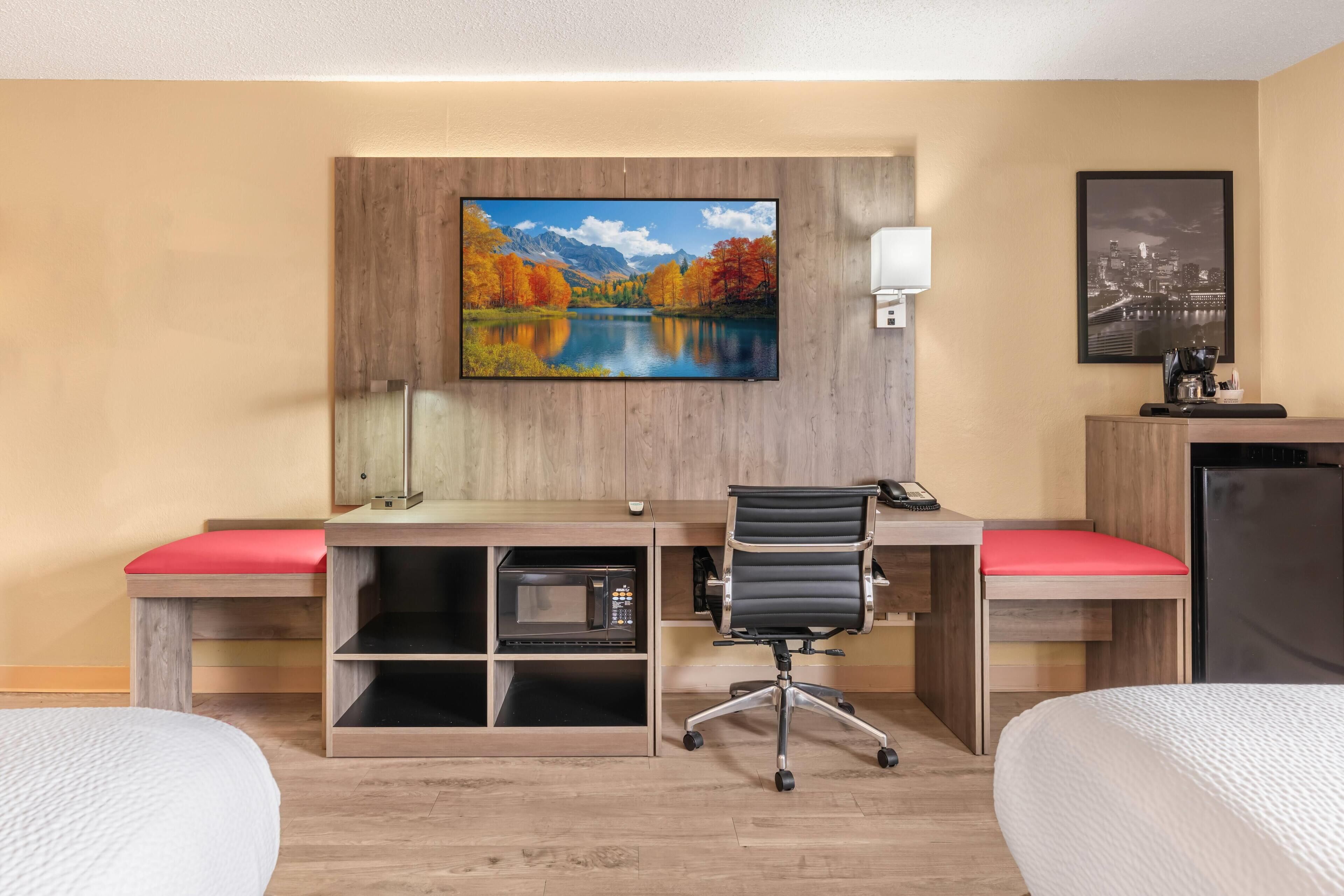 A hotel room with a bed, a desk with a chair, a TV, a microwave, and a refrigerator.