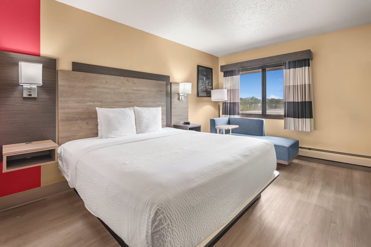 A hotel room with a large bed, bedside tables, a desk, a chair, and a window with curtains.