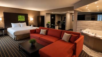 Habitación de hotel con cama, sofá rojo, una mesita con una planta y una pequeña cocina.