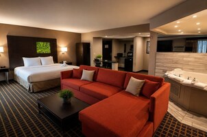 Habitación de hotel con cama, sofá rojo, una mesita con una planta y una pequeña cocina.