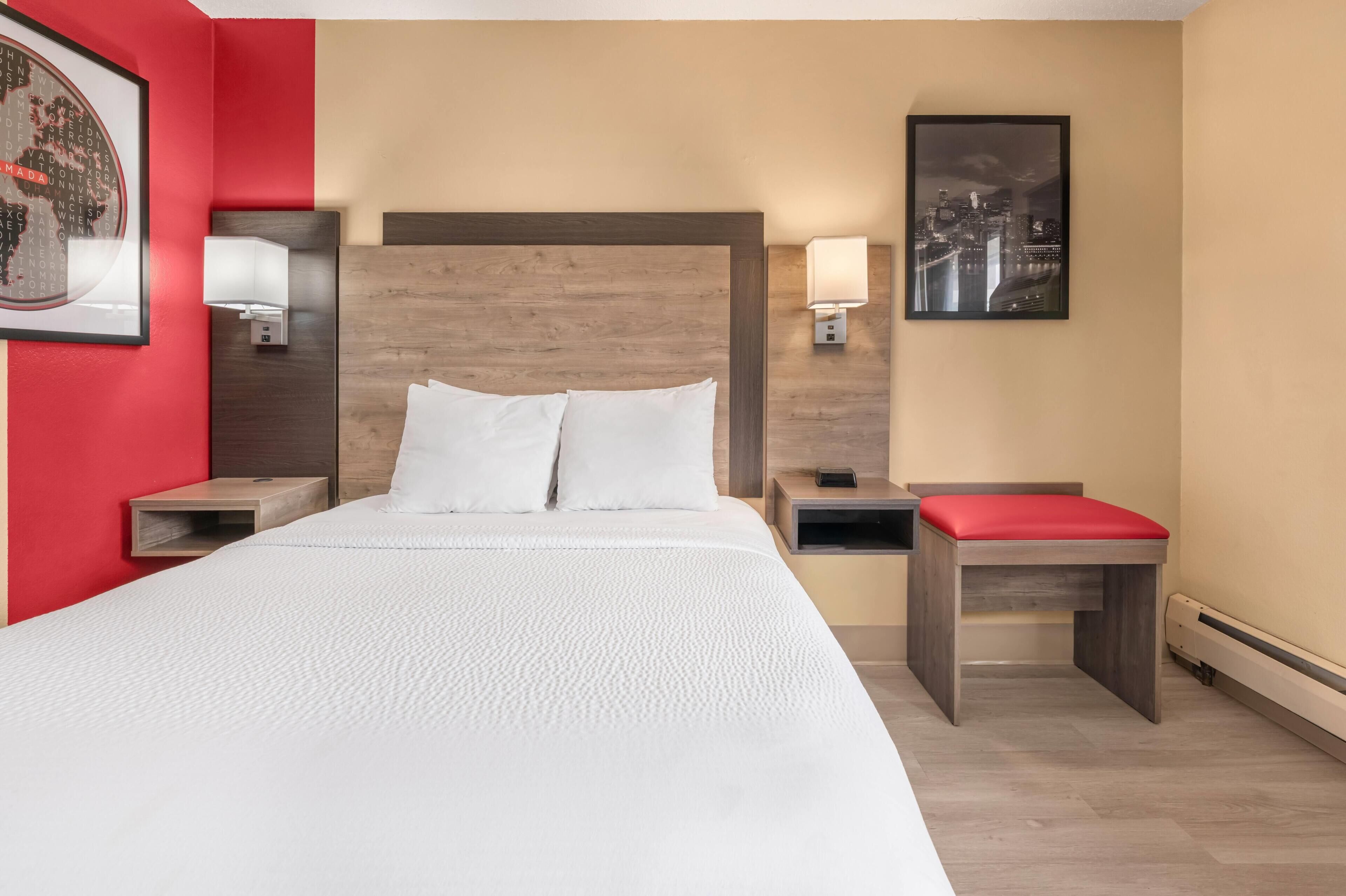 Quarto de hotel com uma cama grande, duas mesas de cabeceira, um banco vermelho, arte de parede com paisagem urbana e um mapa-múndi emoldurado.
