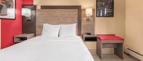 Quarto de hotel com uma cama grande, duas mesas de cabeceira, um banco vermelho, arte de parede com paisagem urbana e um mapa-múndi emoldurado.