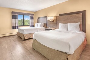 Une chambre d’hôtel avec deux lits, une fenêtre avec des rideaux, une table de chevet et une lampe fixée au mur.