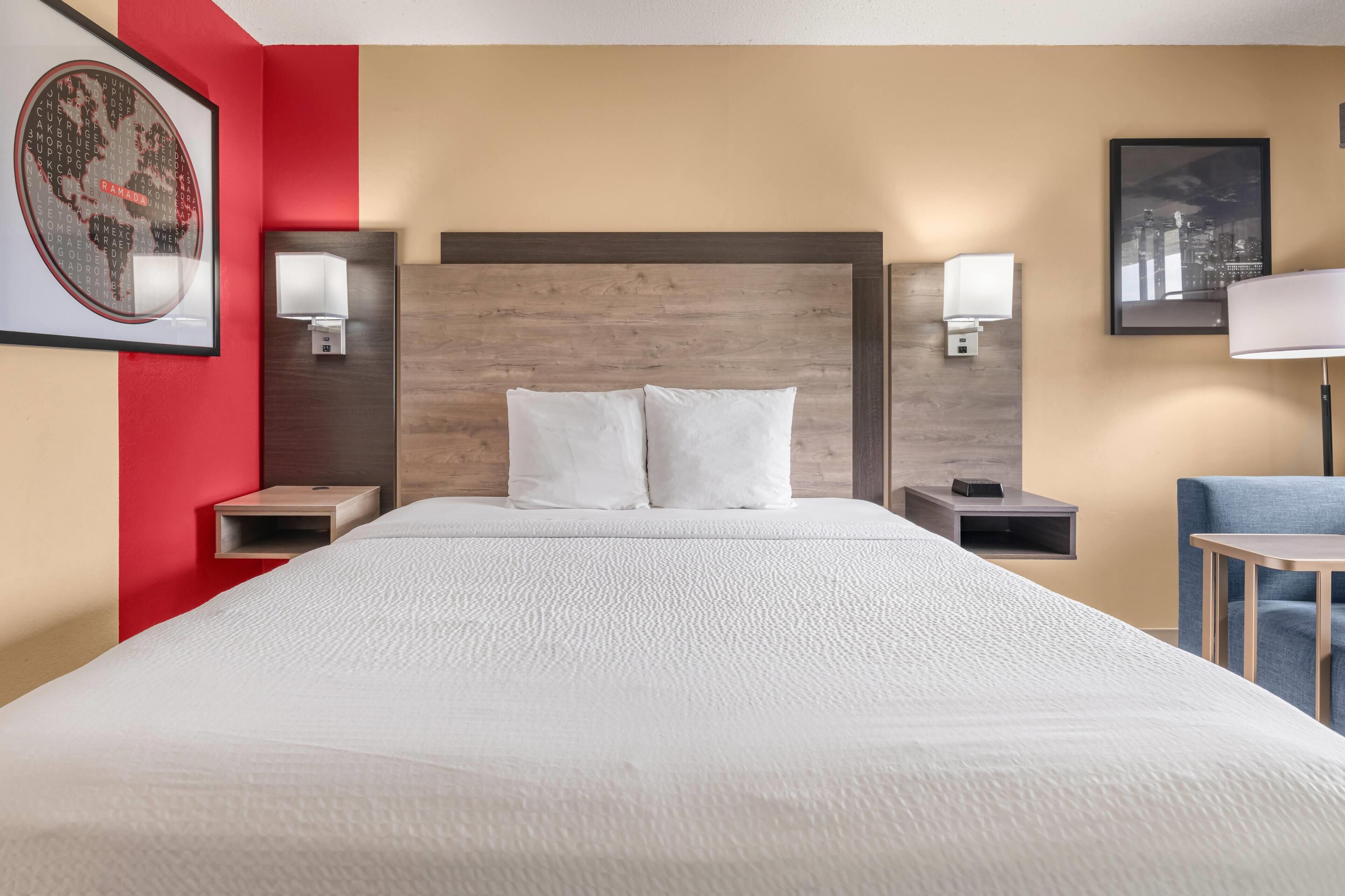 Een hotelkamer met een groot bed, twee nachtkastjes met lampen, een klein tafeltje en een stoel.