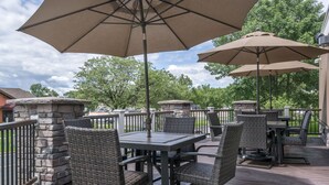 An outdoor patio with stone pillars, wicker chairs, and tables under large umbrellas. - Ramada by Wyndham Minneapolis Golden Valley (Golden Valley)