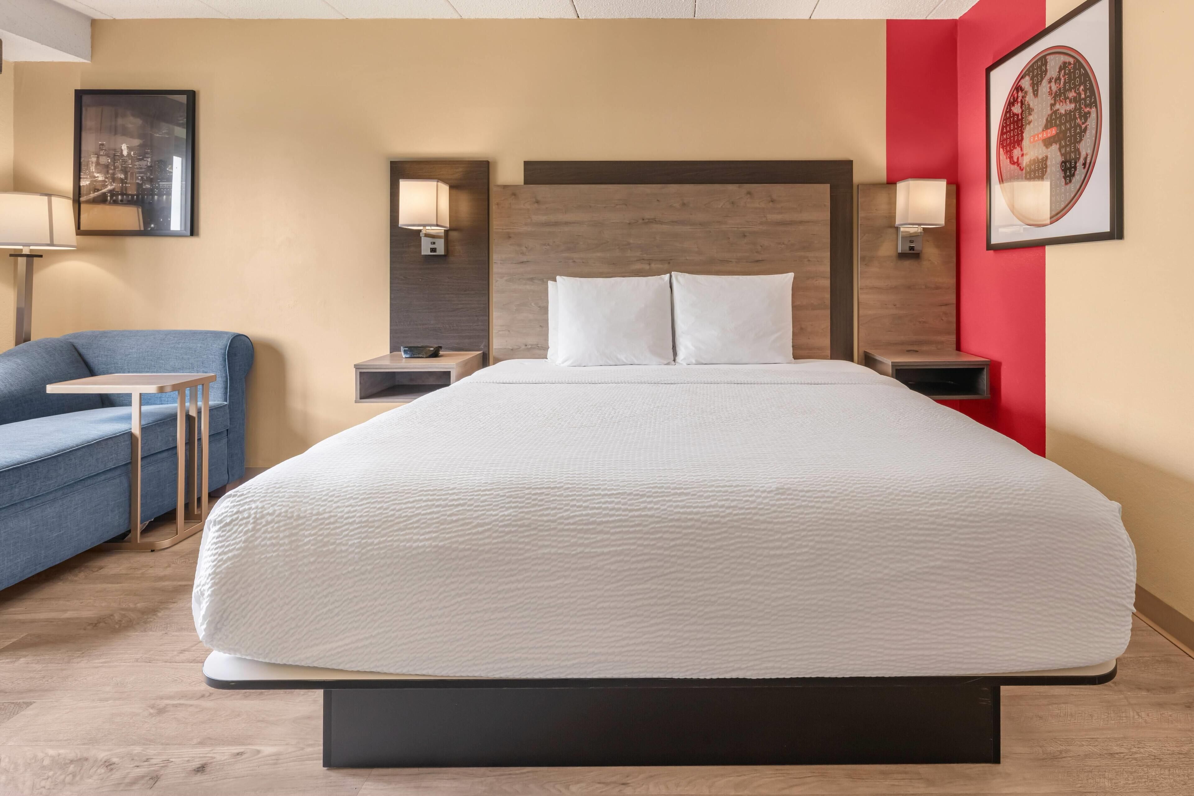 Ein Hotelzimmer mit einem großen Bett, einem blauen Sofa, zwei Nachttischen mit Lampen und einer gerahmten Weltkarte an der Wand.