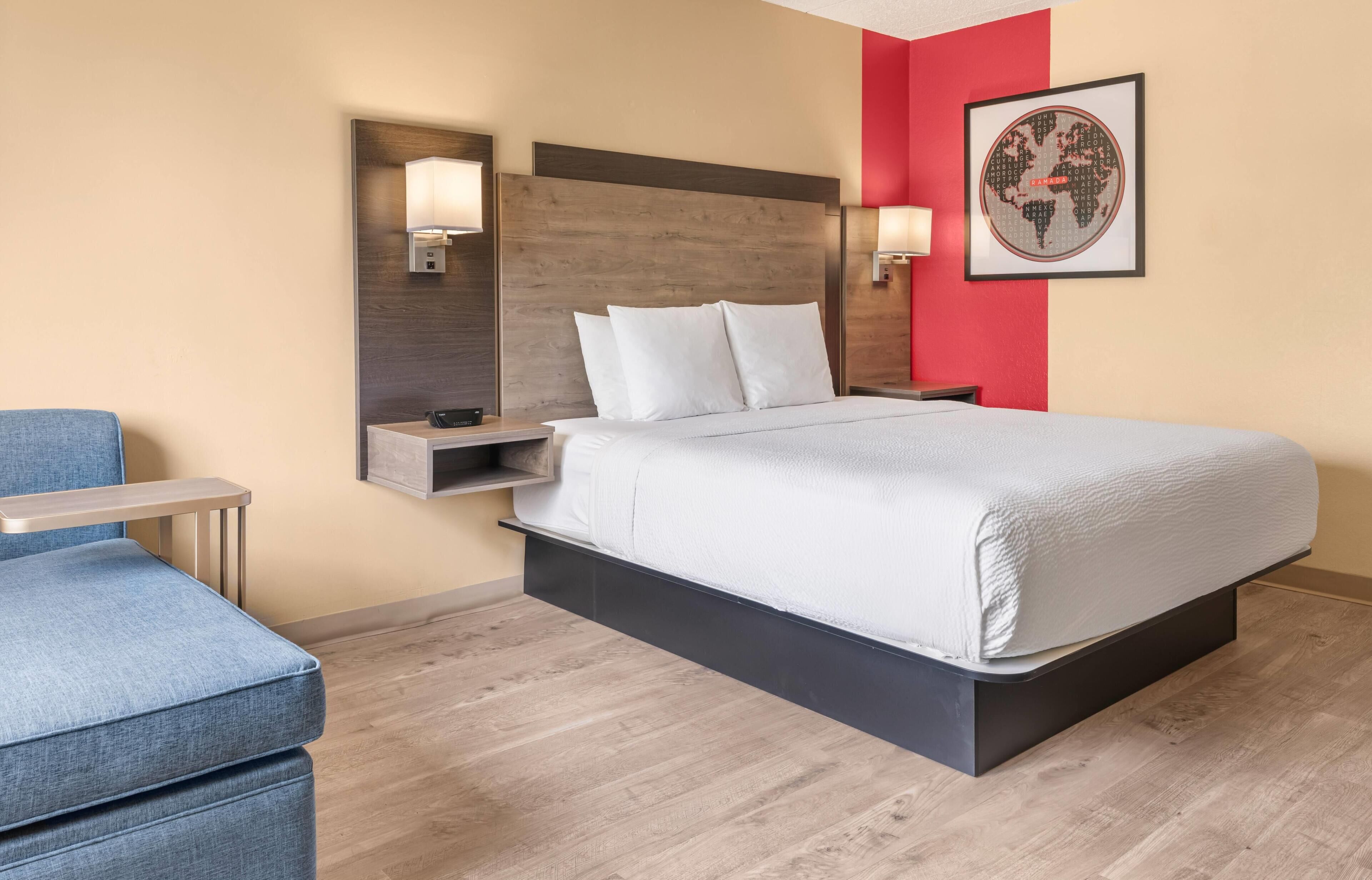 Una habitación de hotel con una cama, mesitas de noche, una silla y una lámpara de pared.
