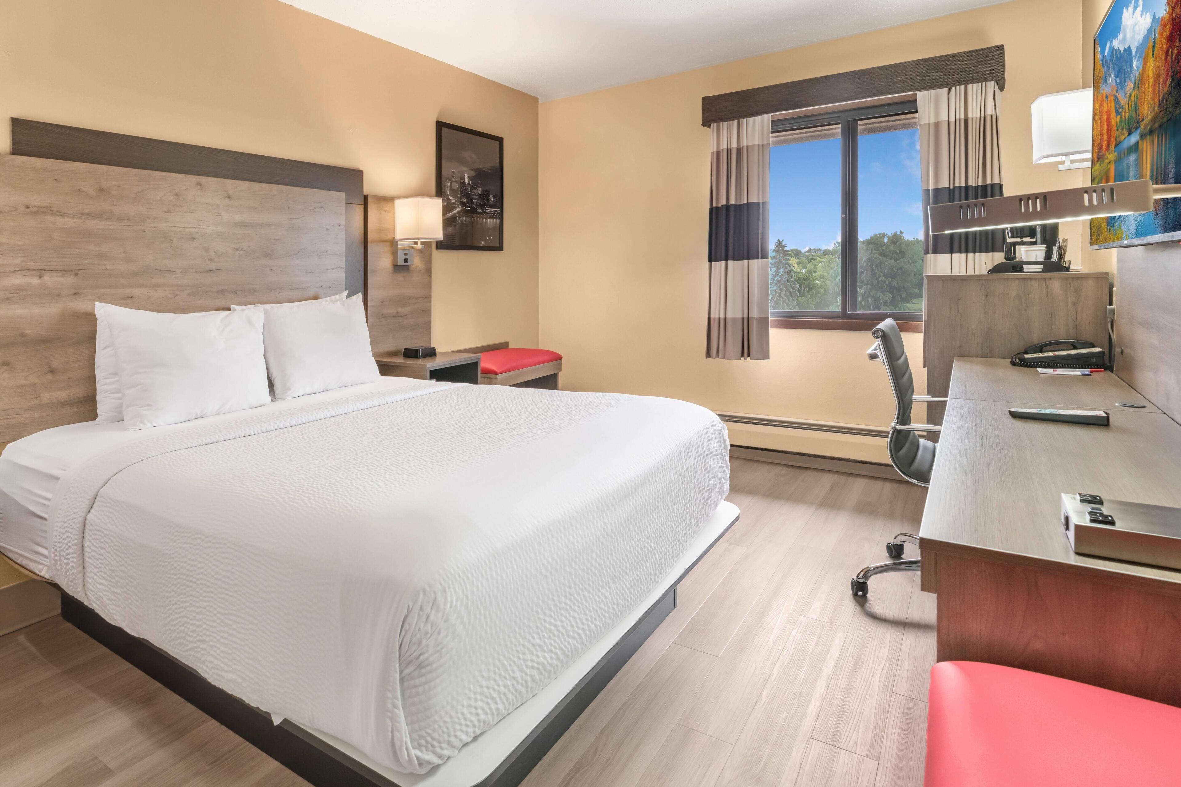 Ein Hotelzimmer mit Bett, Schreibtisch, Stuhl und einem Fenster mit Blick.