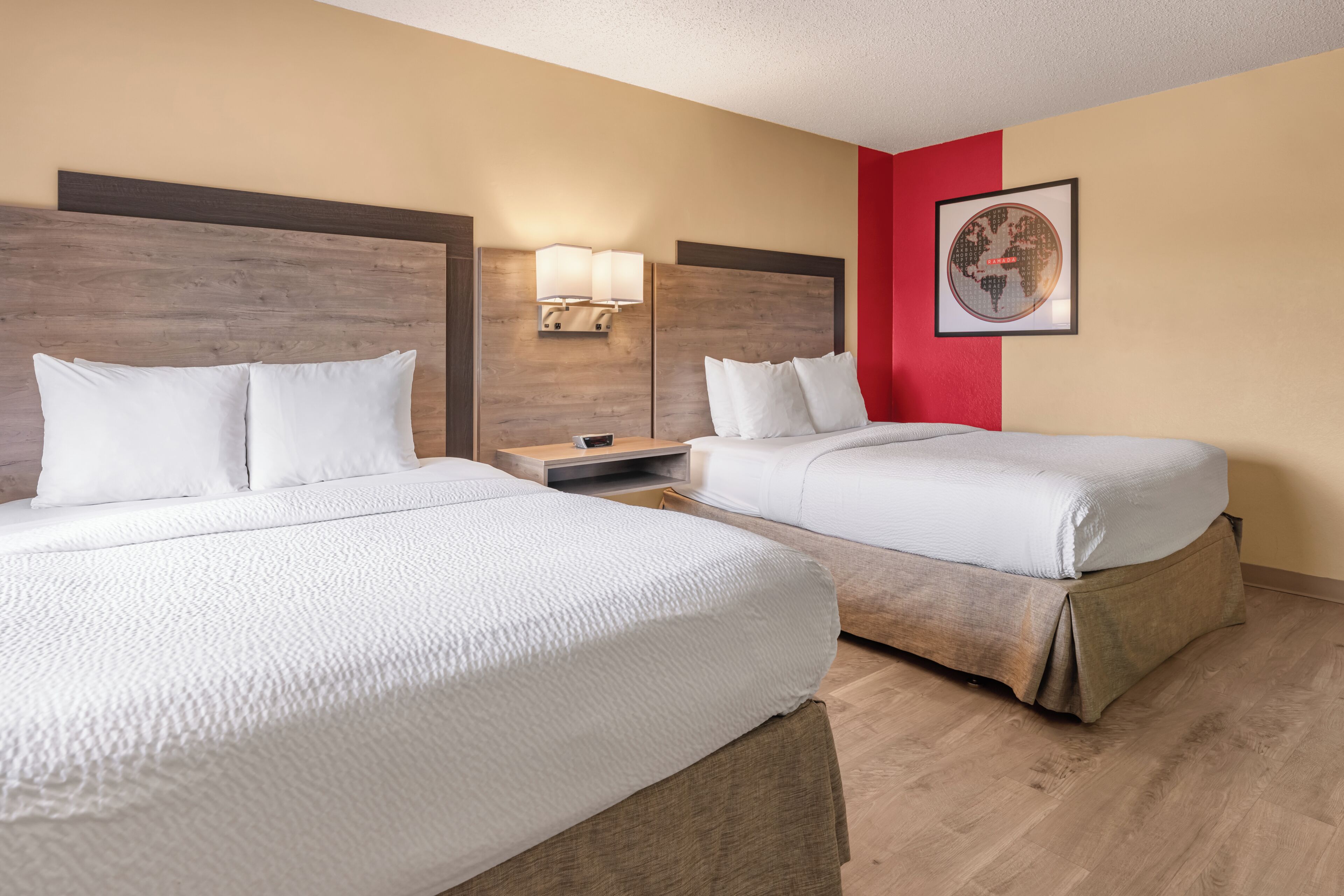 Habitación de hotel con dos camas, cabecero de madera, pared de acento roja y un cuadro enmarcado.