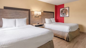 Habitación de hotel con dos camas, cabecero de madera, pared de acento roja y un cuadro enmarcado.
