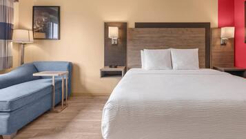 Una habitación de hotel con una cama, un sofá azul, una mesita pequeña y una mesita de noche con lámpara.