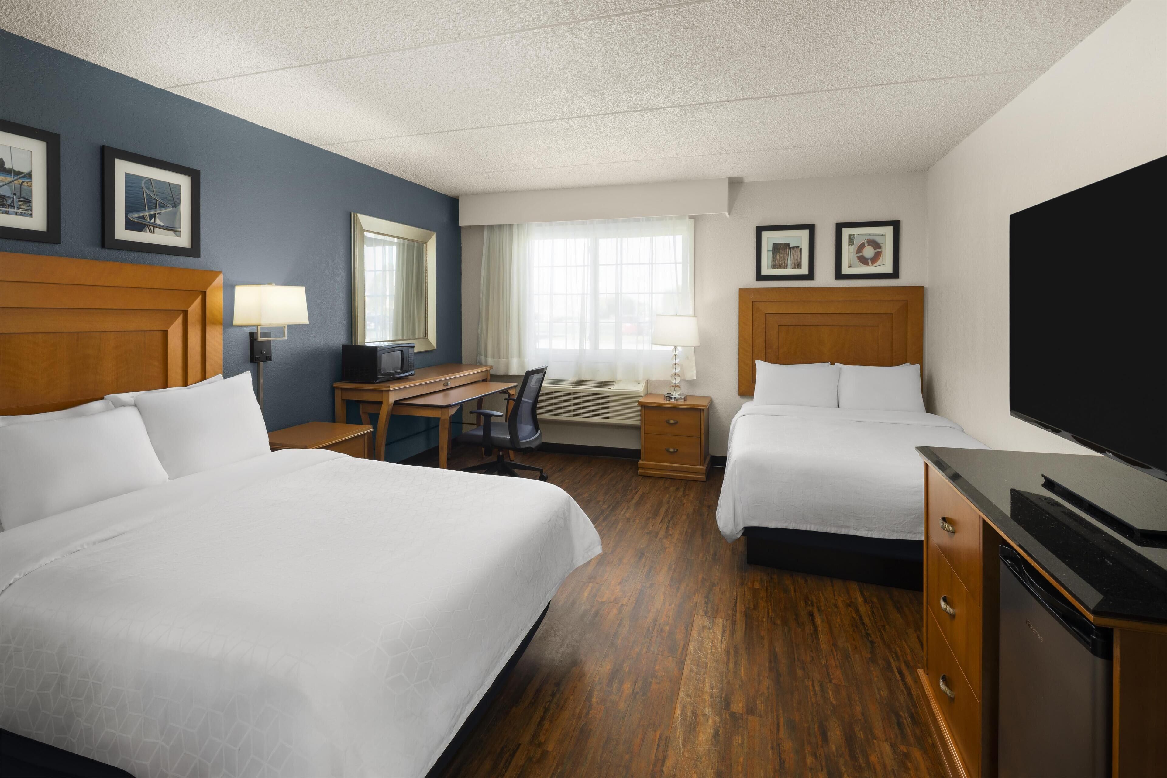 A hotel room with two beds, a desk, a television, and a dresser.