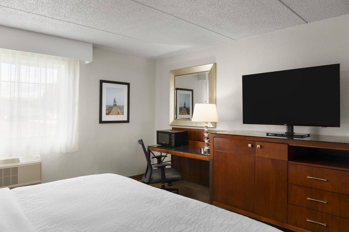 A hotel room with a bed, a desk with a computer, a television, and a window with curtains.