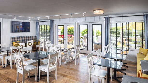 A spacious dining area with white chairs and tables, large windows with blinds, and a view of the outdoors. - Harbor Town, BW Signature Collection (Manitowoc)