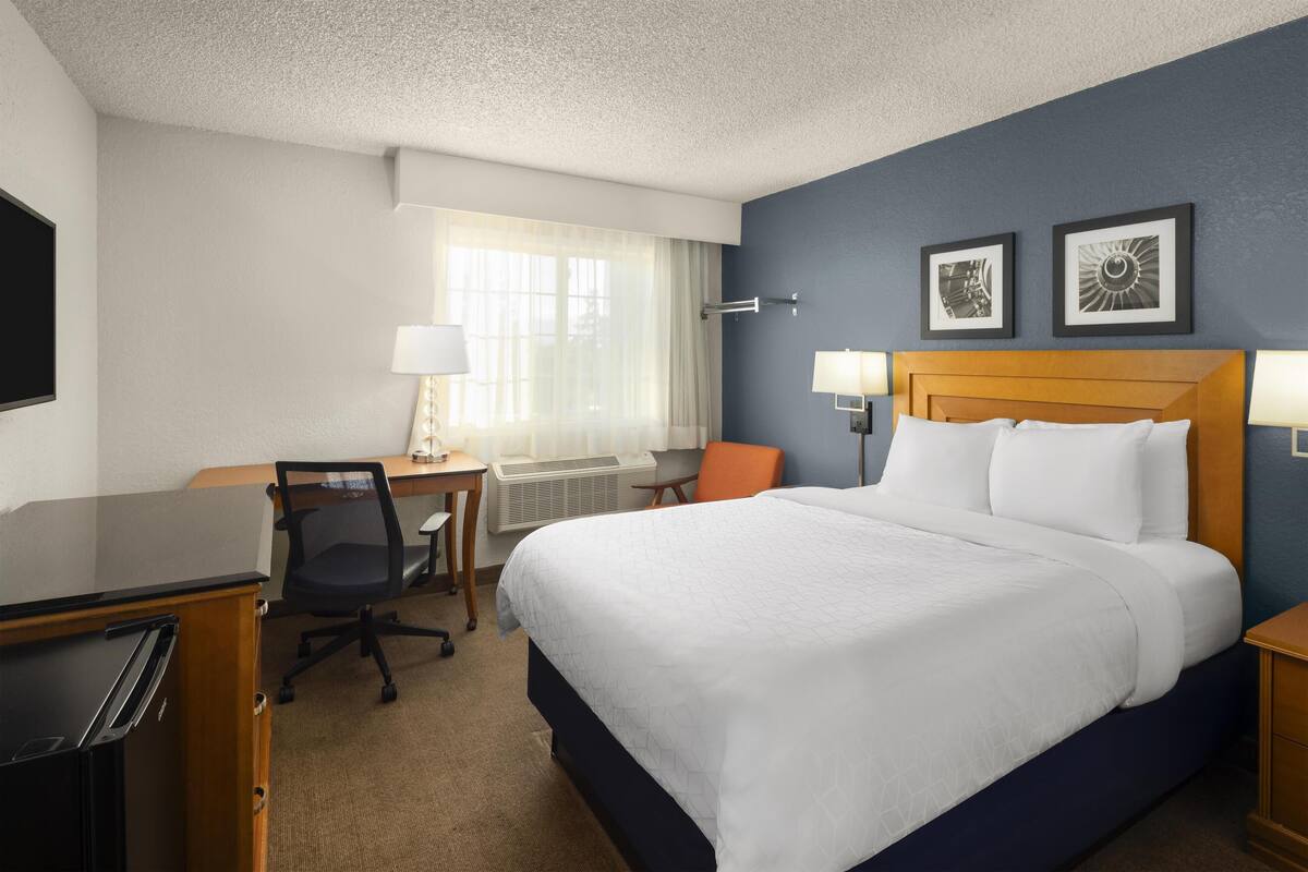 A hotel room with a bed, desk, chair, and two wall-mounted lamps.