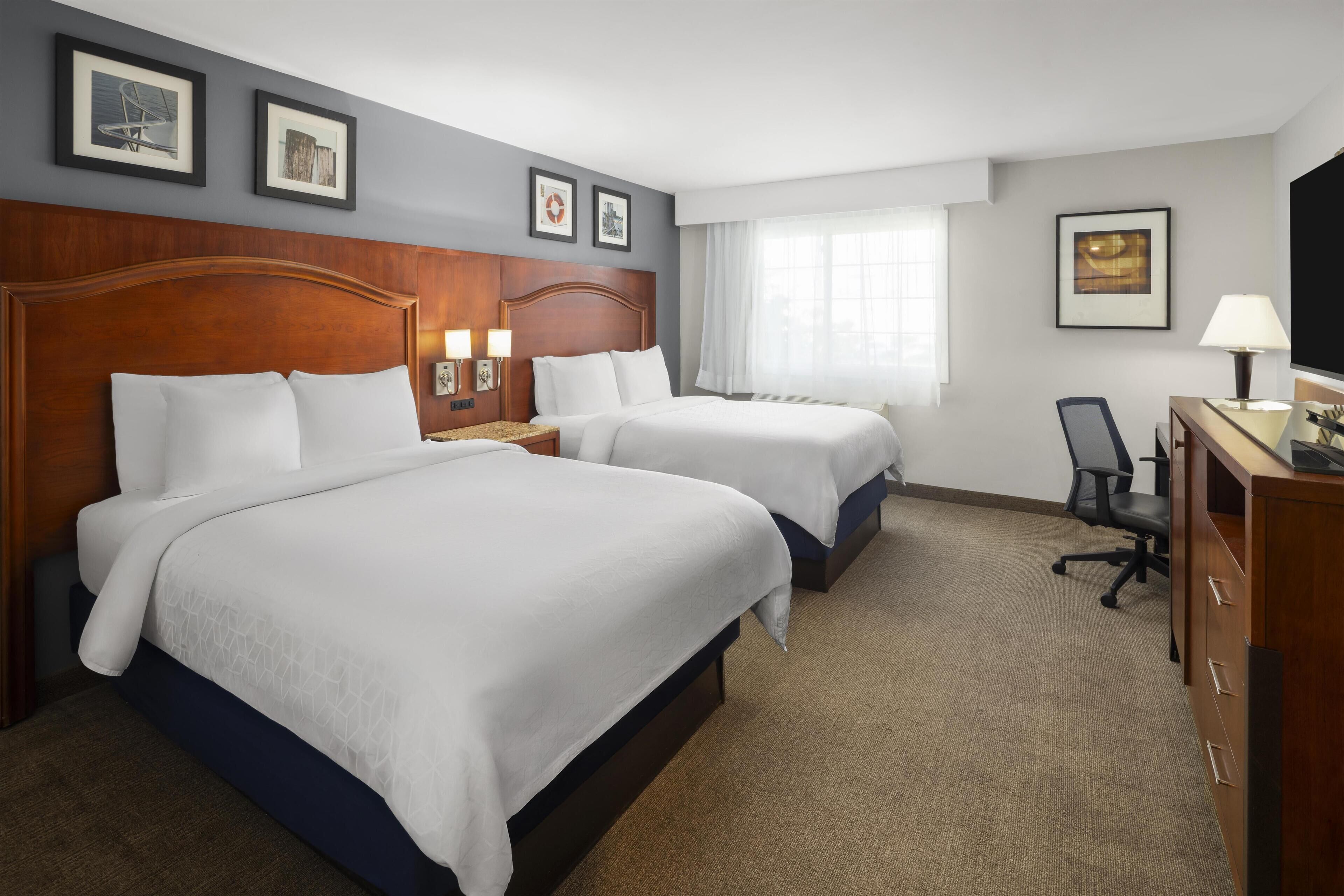 A hotel room with two beds, a desk, a chair, and a TV.