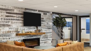 A modern interior with a stone wall, a flat-screen TV, a fireplace, a sofa, and a staircase. - Harbor Town, BW Signature Collection (Manitowoc)