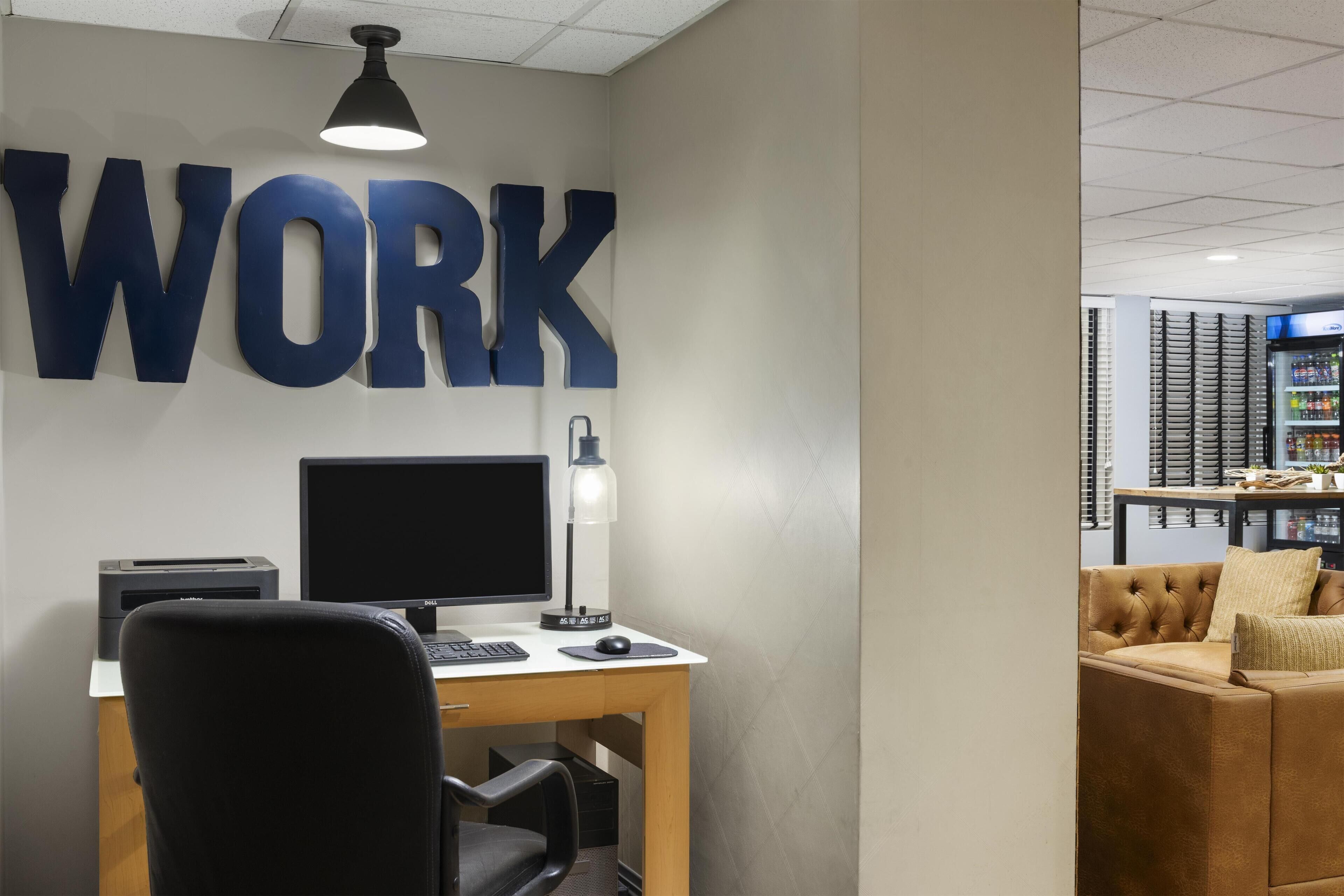 A workspace with a desk, computer, and printer, a large "WORK" sign on the wall, and a couch in the background.