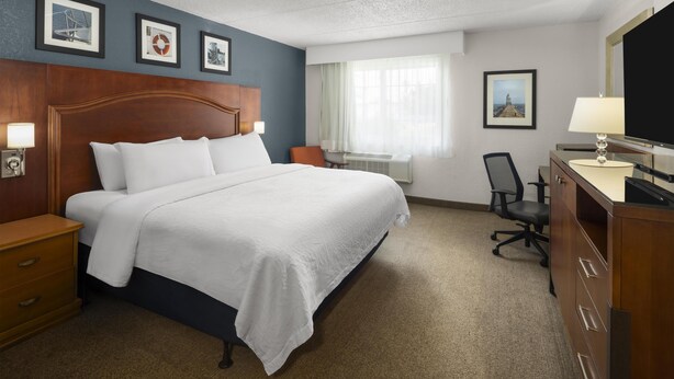 A hotel room with a large bed, a desk with a chair, a dresser, and framed pictures on the wall.