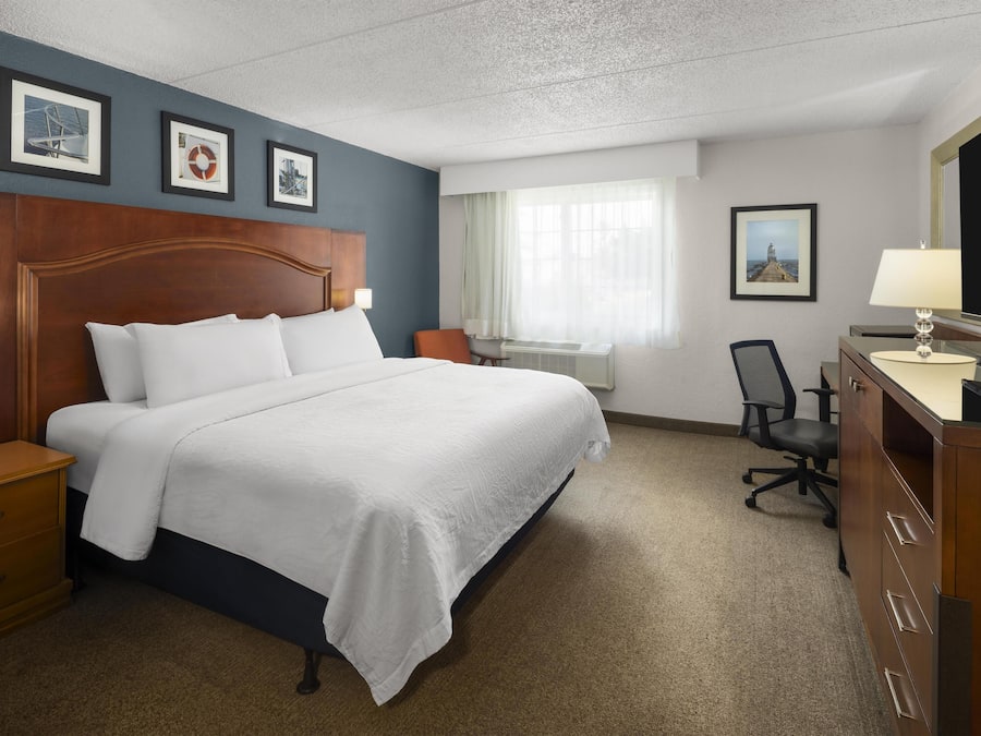Ein Hotelzimmer mit einem großen Bett, einem Schreibtisch mit Stuhl, einem Schminktisch und gerahmten Bildern an der Wand.