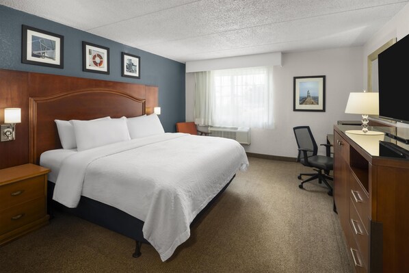 A hotel room with a large bed, a desk with a chair, a dresser, and framed pictures on the wall.