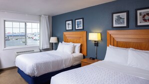 A hotel room with two beds, a window with a view of a parking lot, and two framed pictures on the wall.