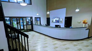 A reception area with a curved counter, a staircase, and a view of the outside through glass doors. - Woodfield Inn and Suites (Marshfield)
