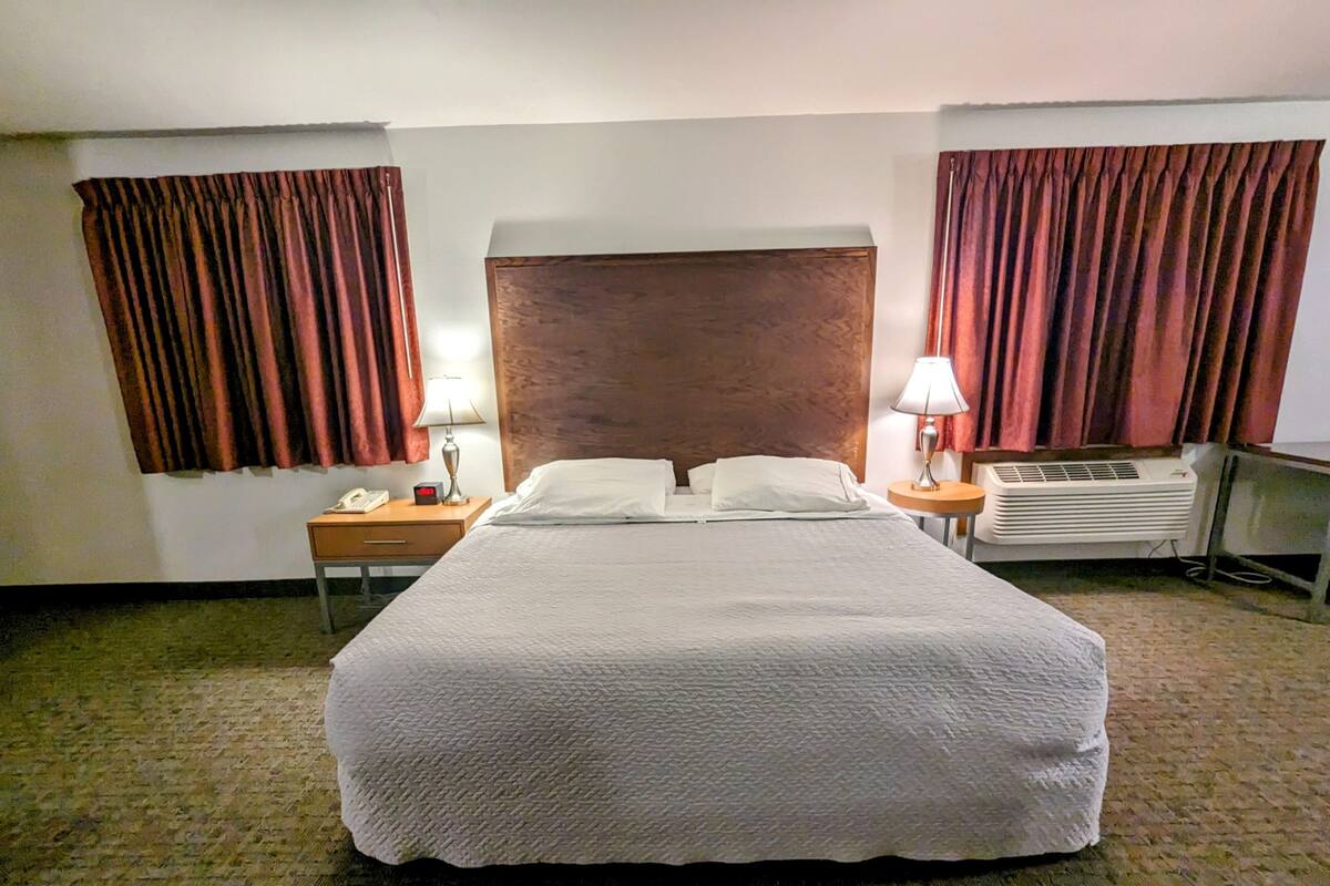 A hotel room with a large bed, two bedside tables with lamps, a telephone, and an air conditioning unit.