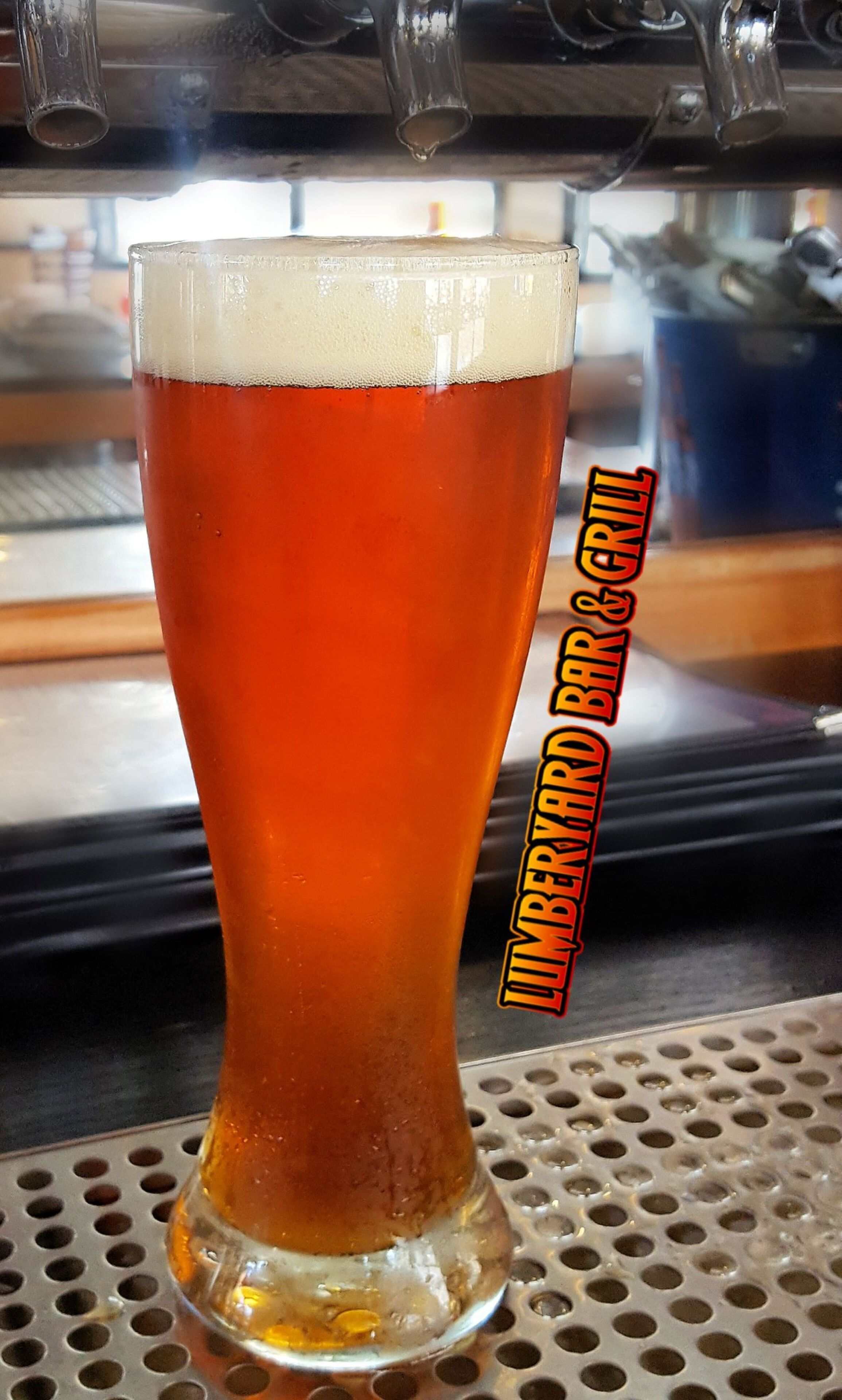 Una jarra alta de cerveza con espuma, sobre una superficie de metal perforado.