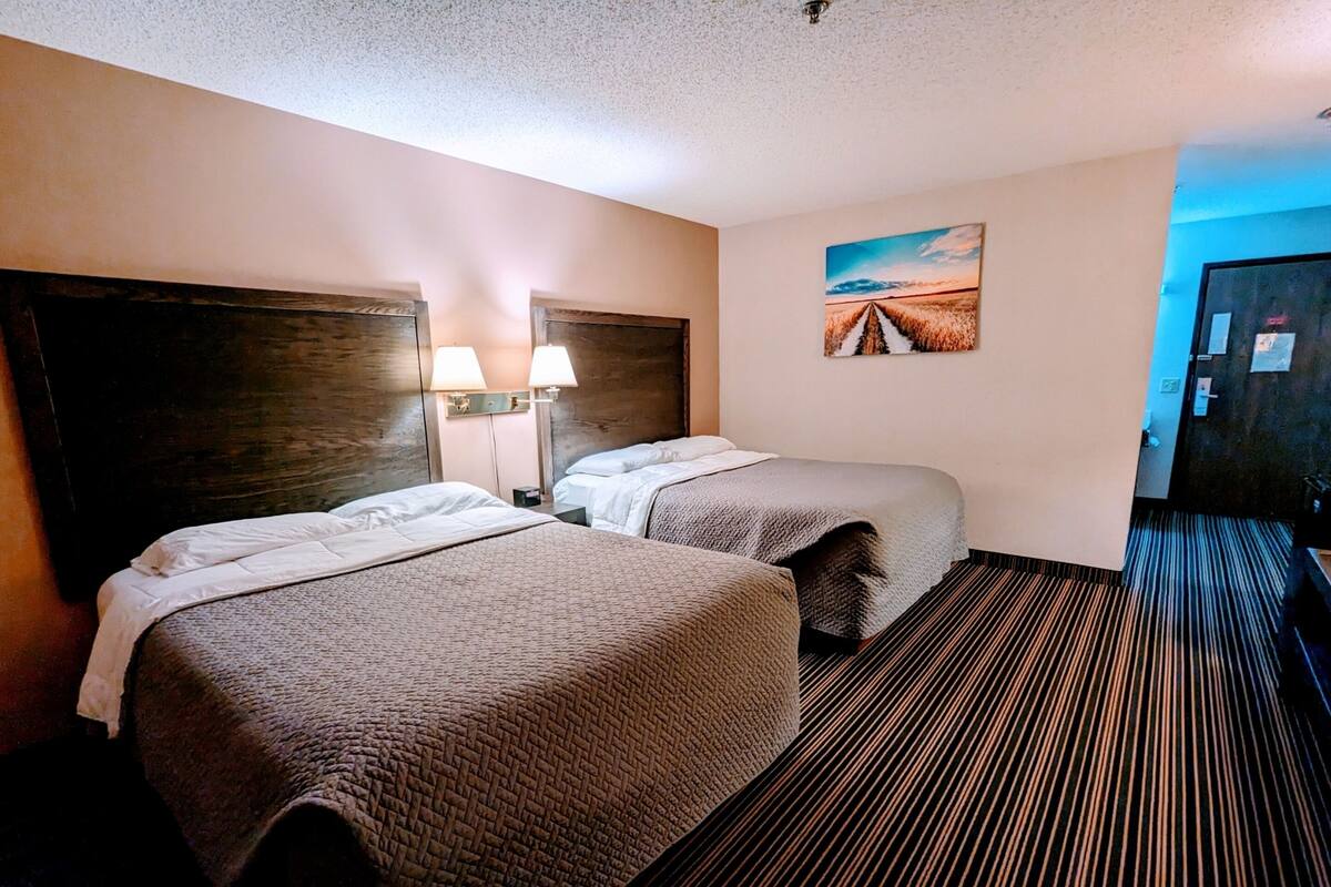 A hotel room with two beds, a large painting on the wall, and a striped carpet.