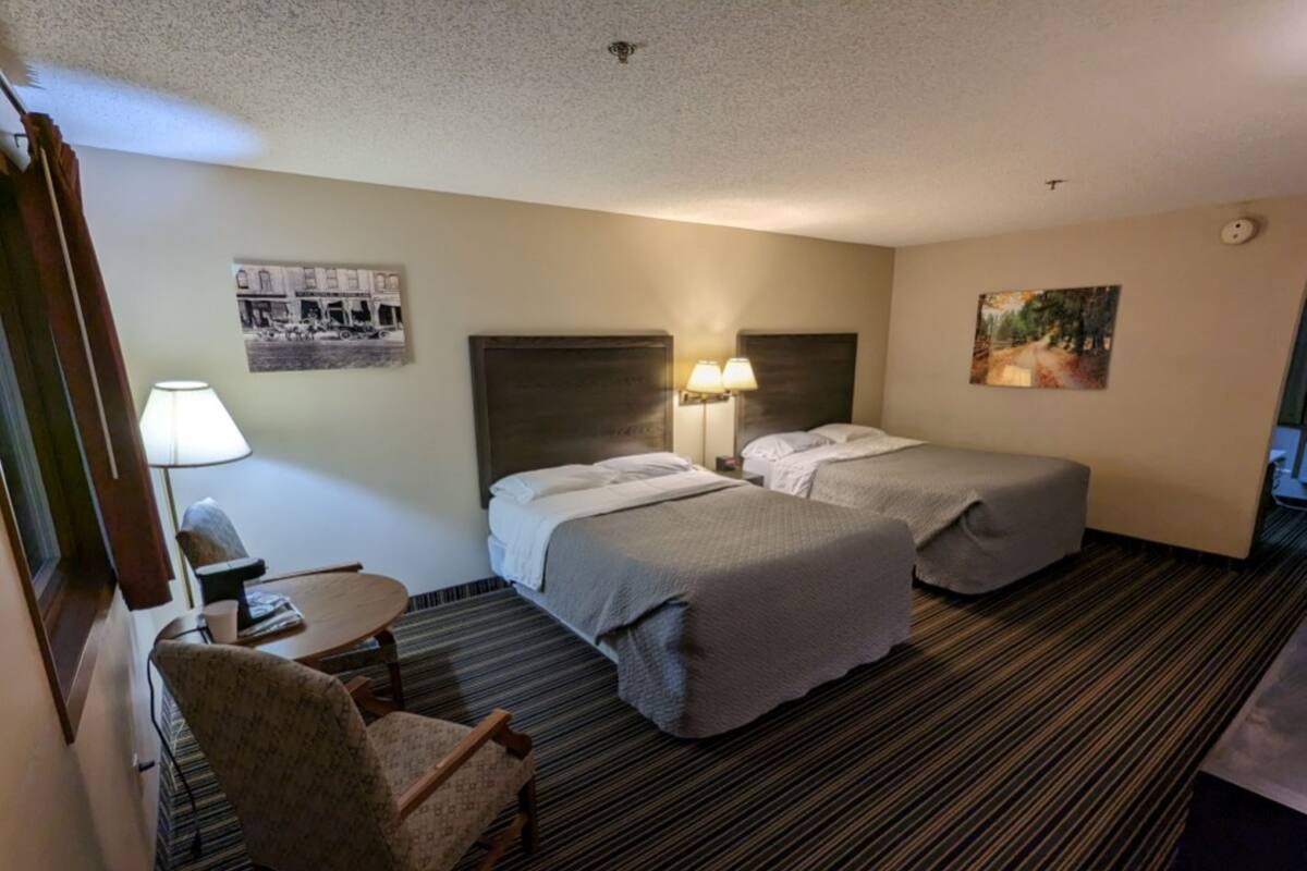 A hotel room with two beds, a chair, a desk, and a lamp.