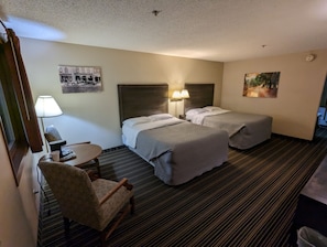 A hotel room with two beds, a chair, a desk, and a lamp. - Woodfield Inn and Suites (Marshfield)